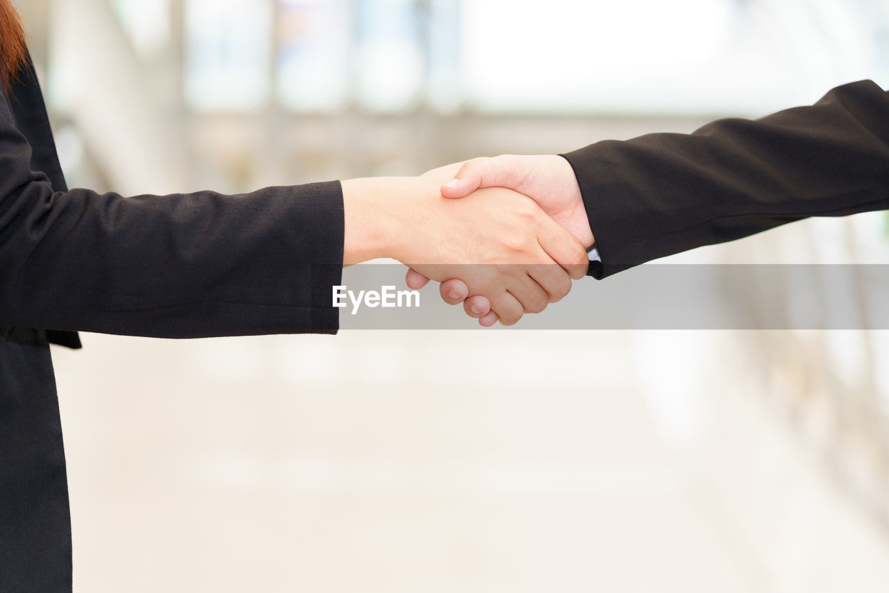 Cropped image of businesswomen shaking hands while standing in office
