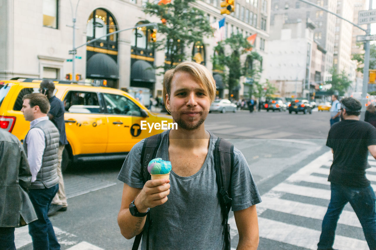 Portrait of smiling young man holding ice cream against buildings in city