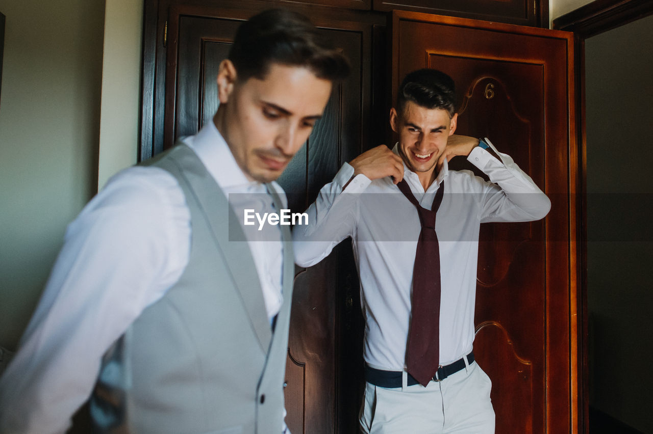 Groom and friend getting dressed at home