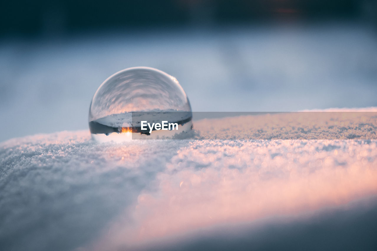 Glass transparent ball in the snow in winter, sun rays reflection. severe frost, cold