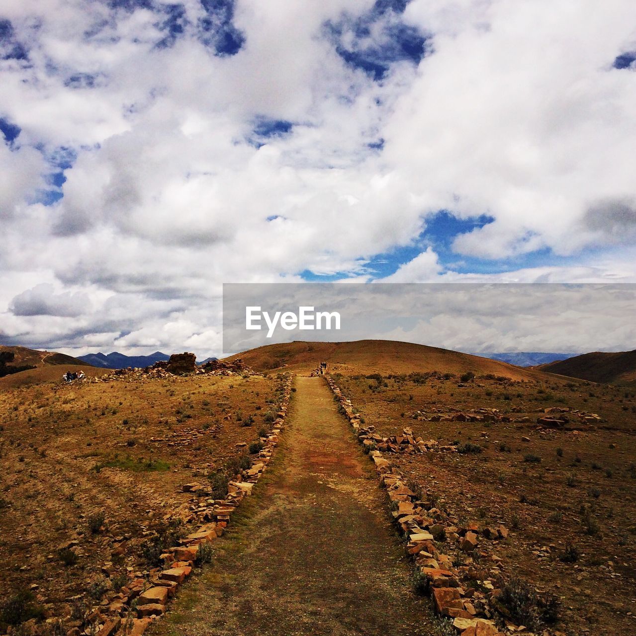 Pathway leading towards hill against cloudy sky
