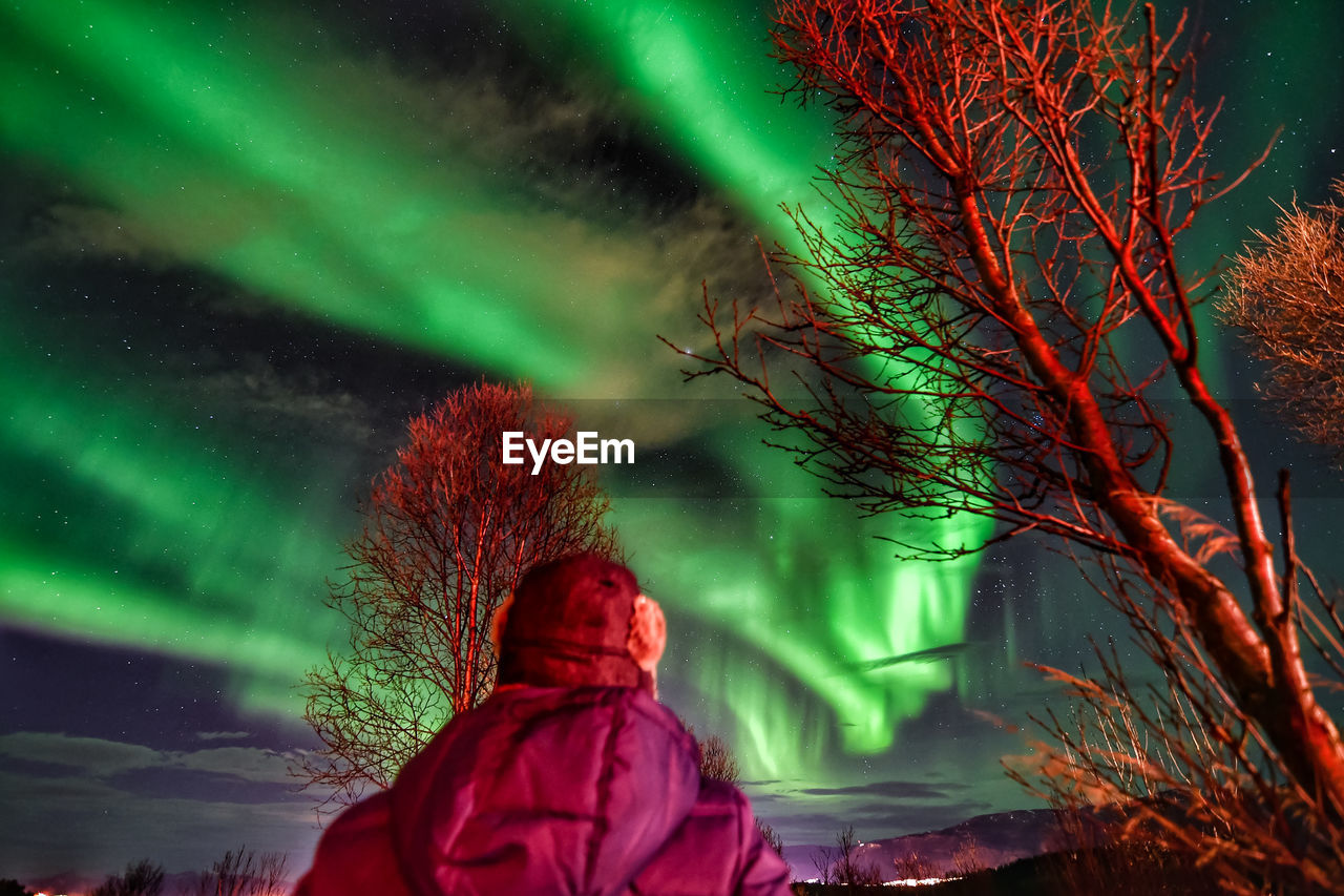 Rear view of mature man looking at aurora borealis in sky at night