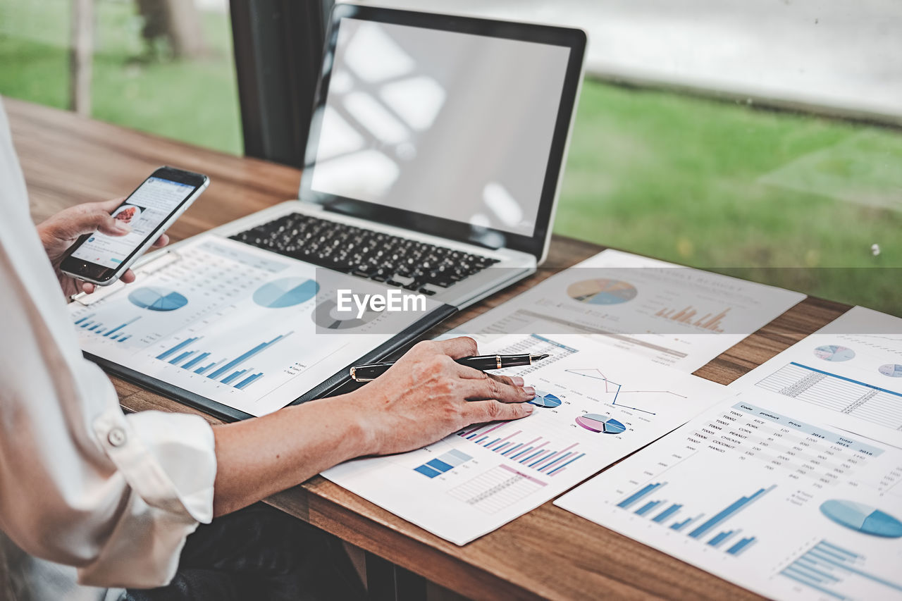 Midsection of businessman using phone while working over graph on table