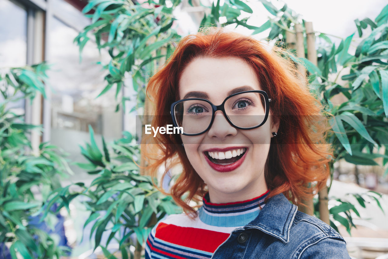 Portrait of smiling redhead young woman against plant