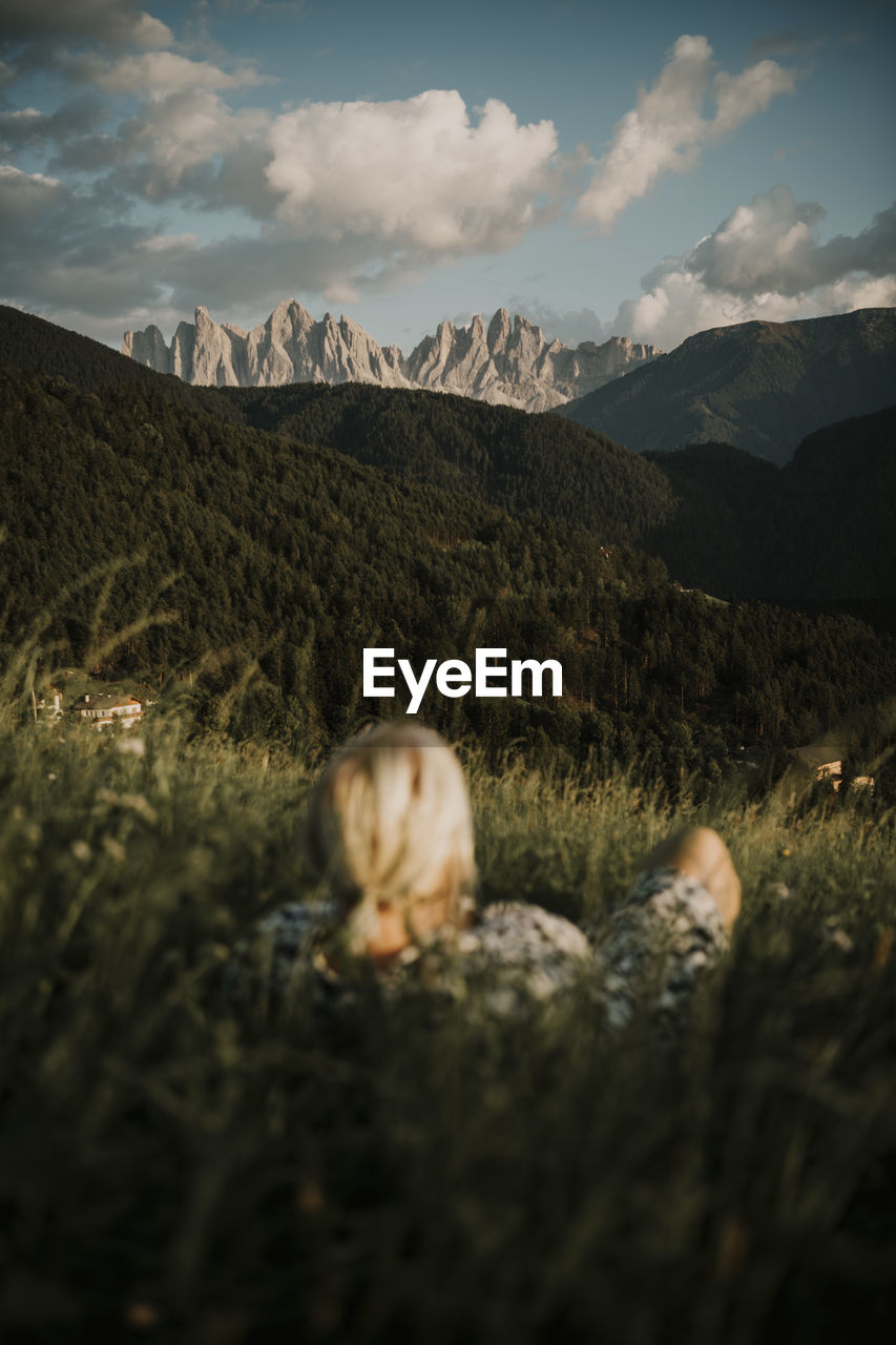 Woman lying on grass while looking at dolomites mountain ranges in south tyrol, italy