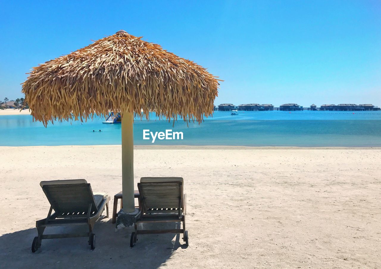 Deck chairs on beach against clear blue sky