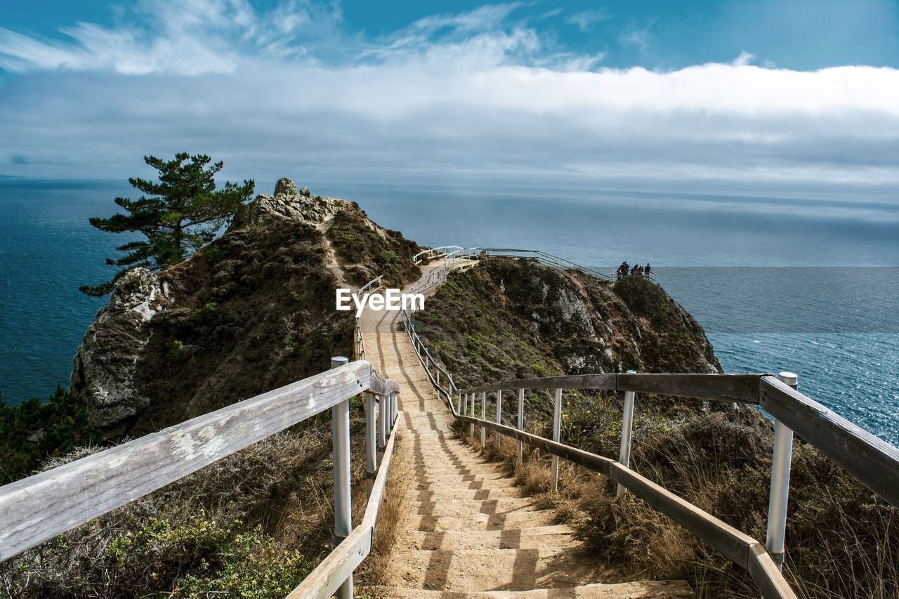High angle view of staircase on mountain leading towards sea against cloudy sky
