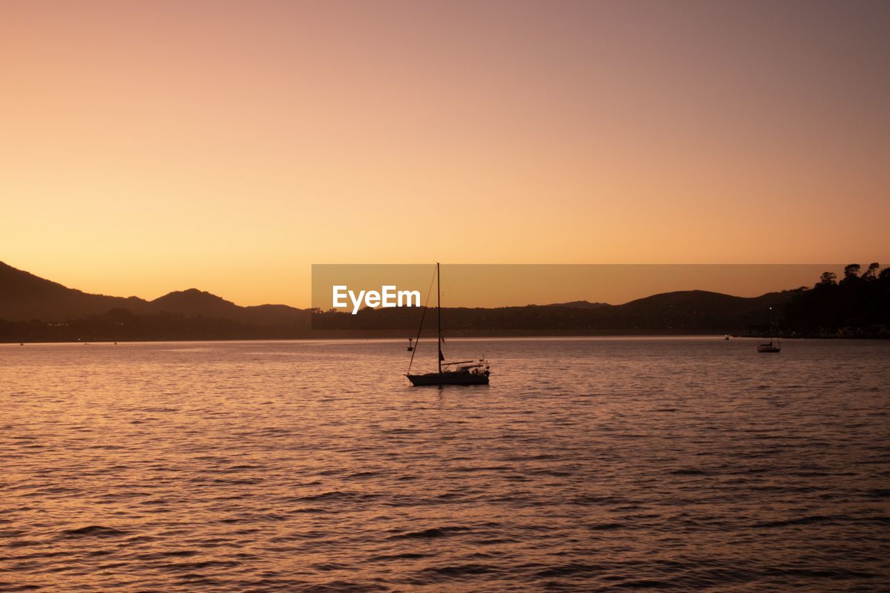 Silhouette sailboat in sea against sky during sunset