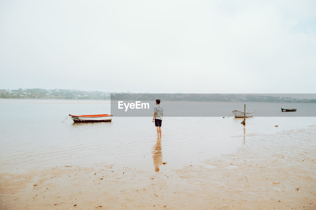 Rear view of man standing on beach against sky