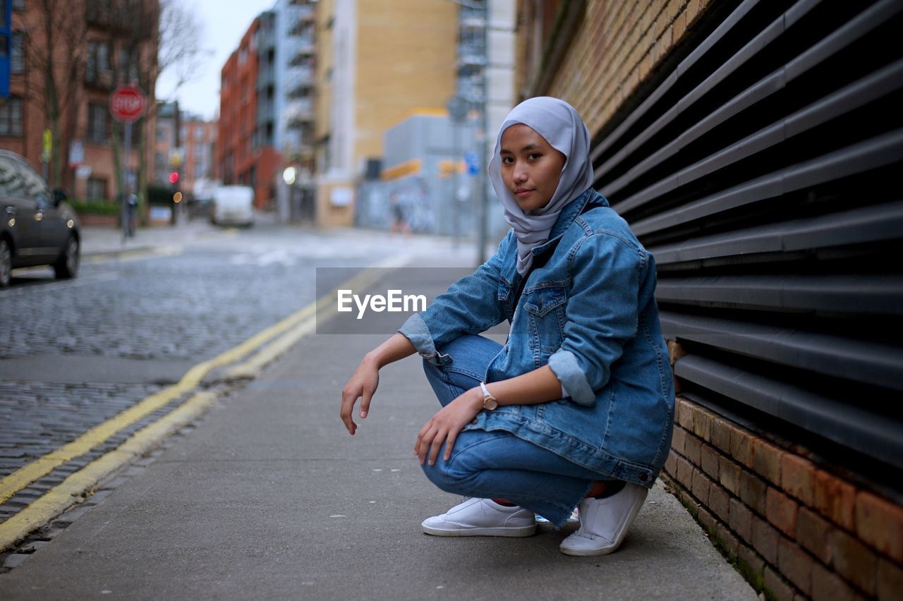 Portrait of woman in hijab crouching on footpath