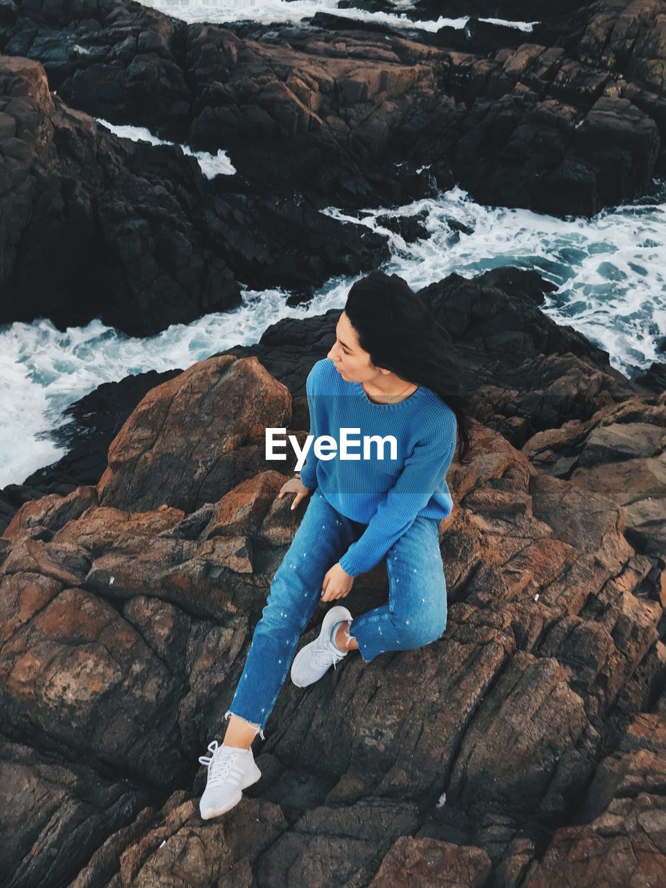 HIGH ANGLE VIEW OF WOMAN SITTING ON ROCKS