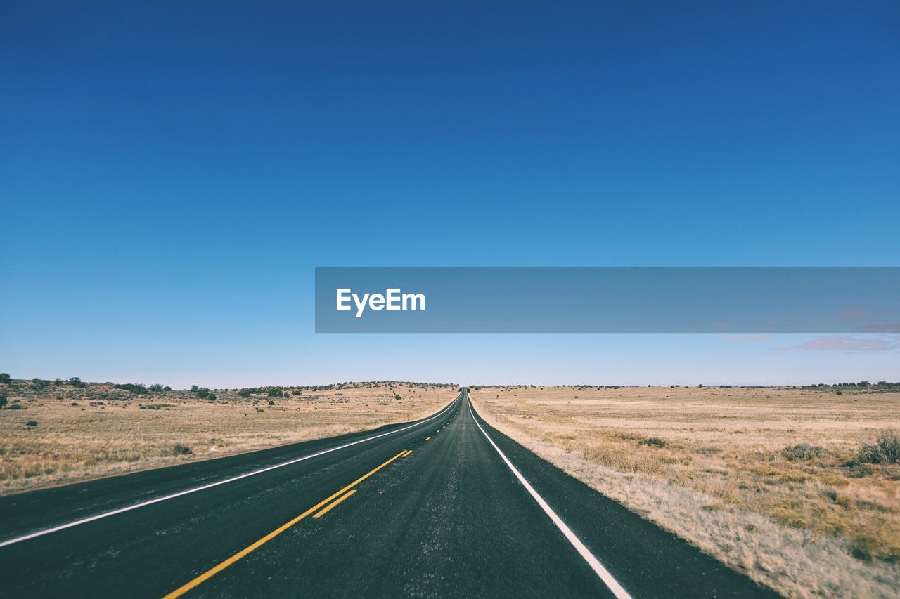 Road by landscape against clear blue sky