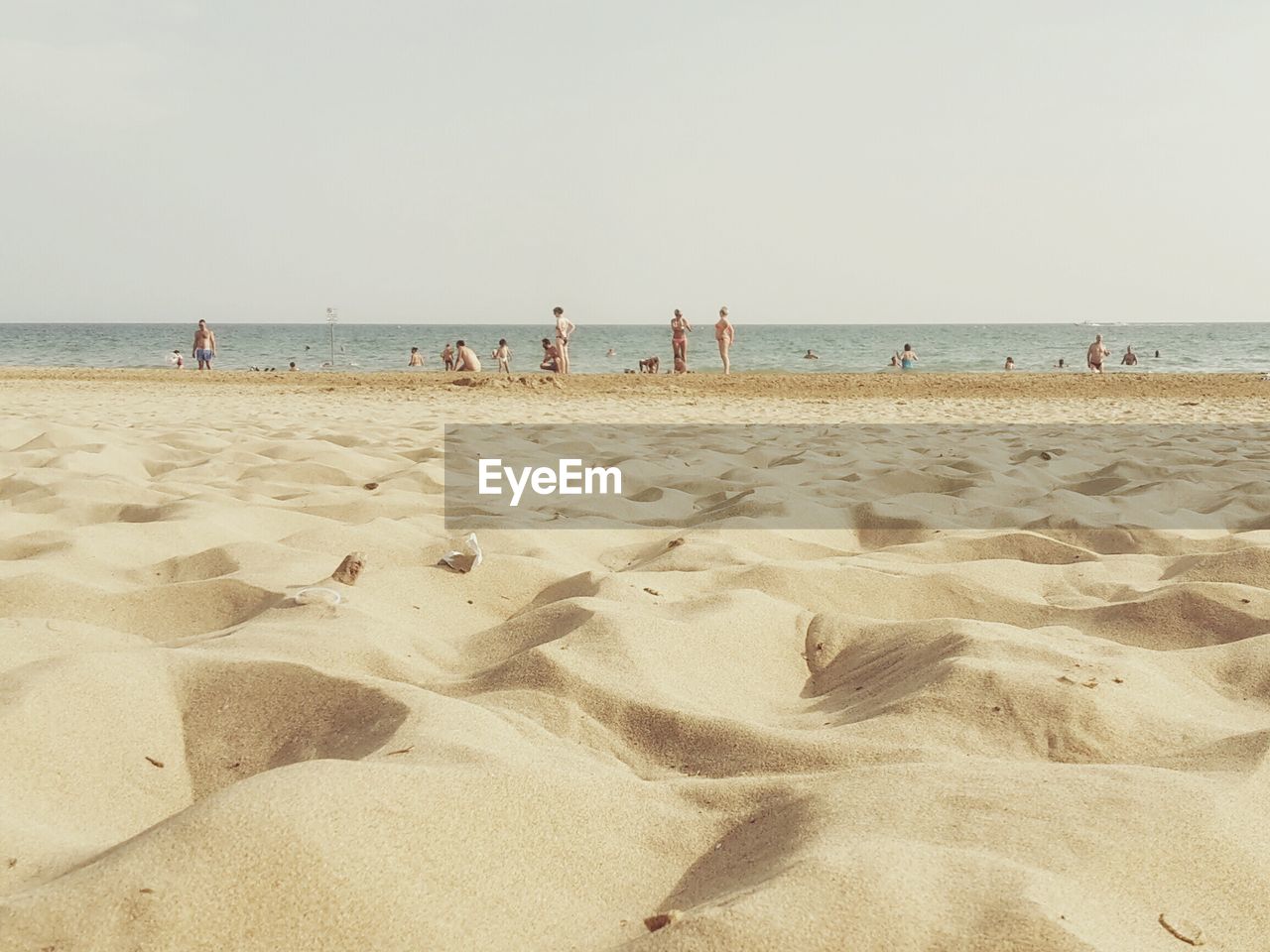 Surface level view of sand with people at beach against clear sky