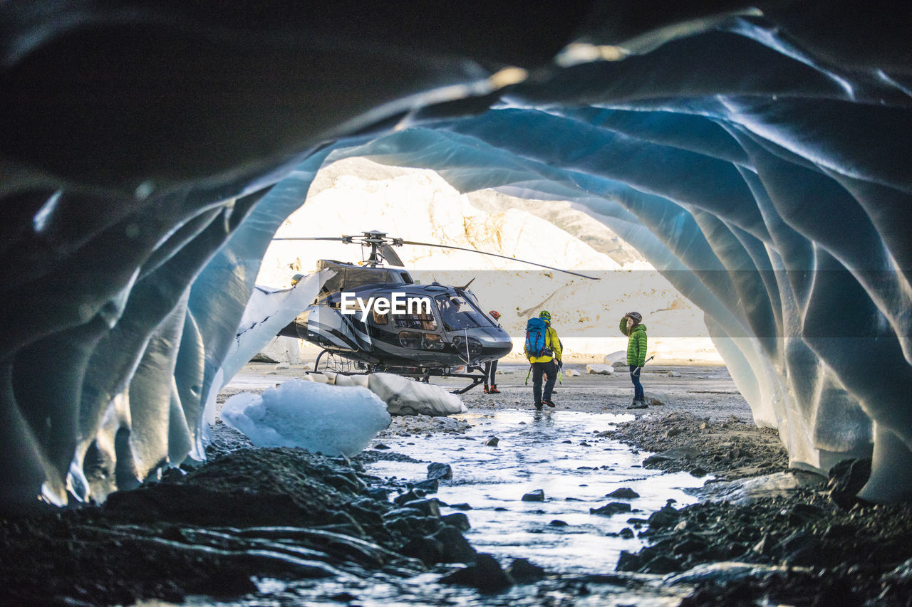 Couple approaches helicopter after exploring ice cave.