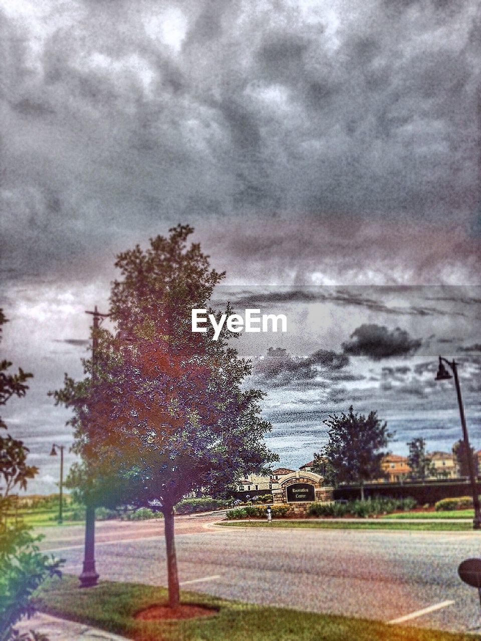 ROAD PASSING THROUGH TREES AGAINST CLOUDY SKY