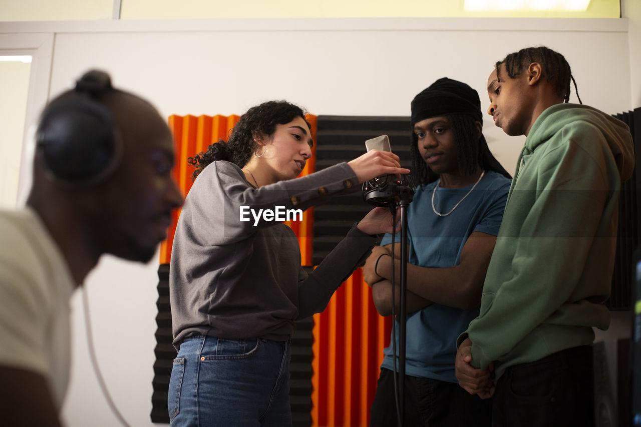 Woman adjusting microphone while rappers standing in studio