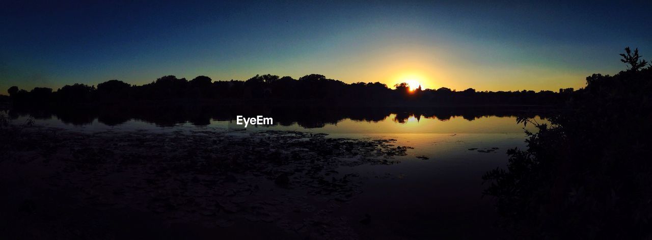 REFLECTION OF SILHOUETTE TREES ON LAKE AGAINST SKY