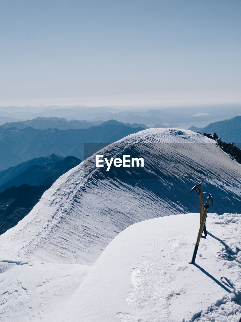 Ice axes on snowcapped mountain against clear sky