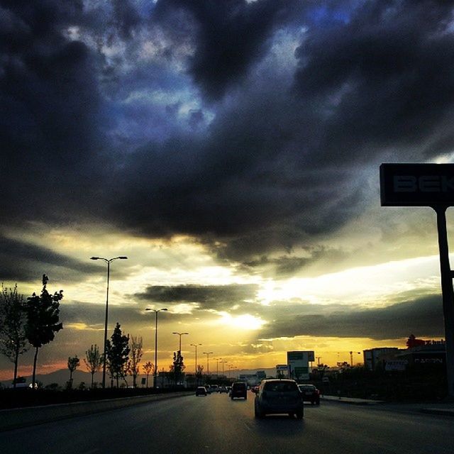 cloud, sky, transportation, car, mode of transportation, motor vehicle, road, dusk, sunset, evening, street, sign, dramatic sky, nature, storm, land vehicle, darkness, city, horizon, light, storm cloud, no people, afterglow, sunlight, cloudscape, architecture, traffic, road sign, outdoors, silhouette, street light, travel, highway, motion, tree, overcast