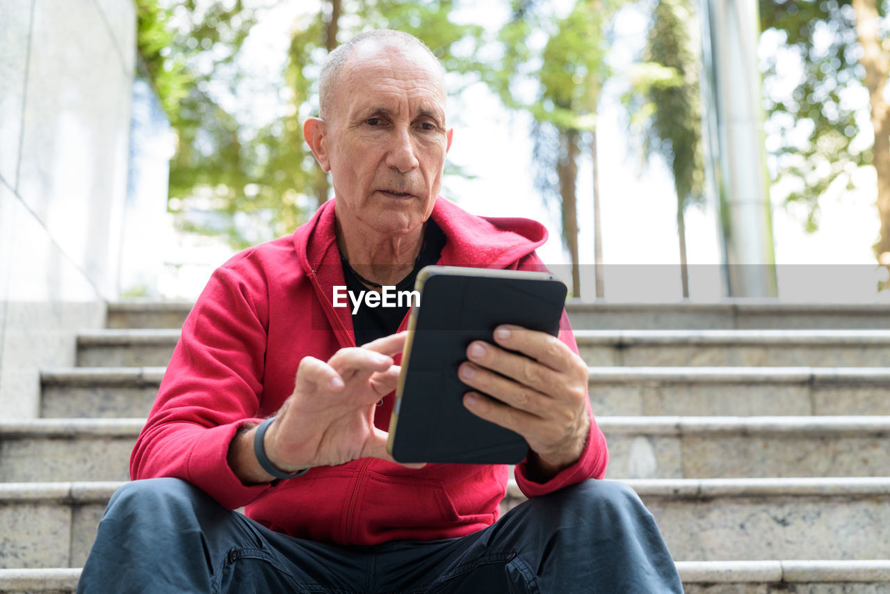 MID ADULT MAN USING MOBILE PHONE WHILE SITTING ON STAIRCASE