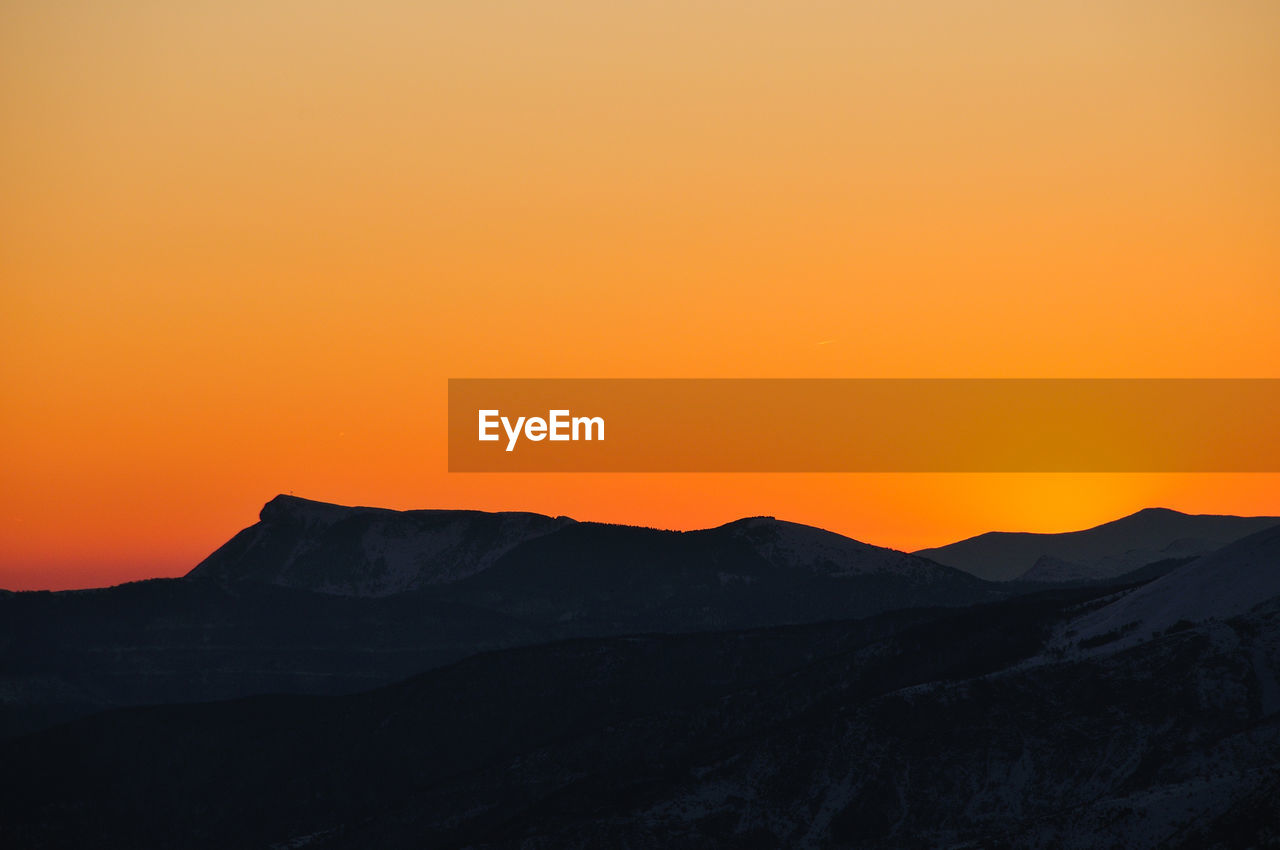 Scenic view of silhouette mountains against orange sky