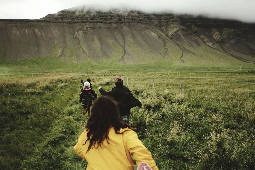 REAR VIEW OF WOMEN ON GRASSY FIELD AGAINST SKY