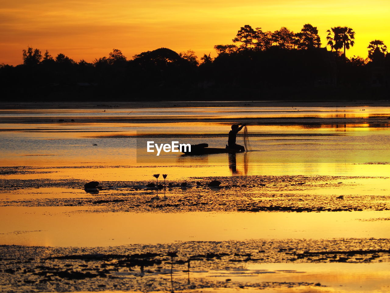 Silhouette man fishing in lake during sunset