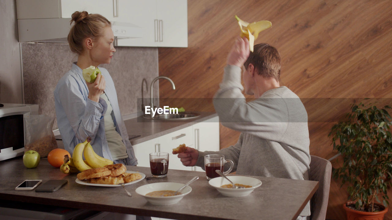 Man throwing banana while talking with wife at kitchen