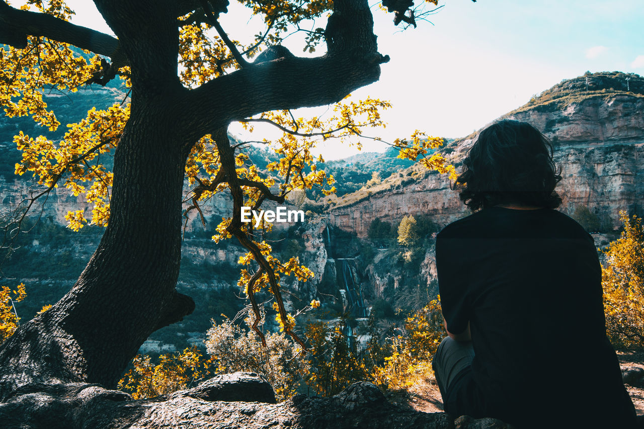 A girl with her back sitting under the shade of a tree enjoying the landscape relaxed