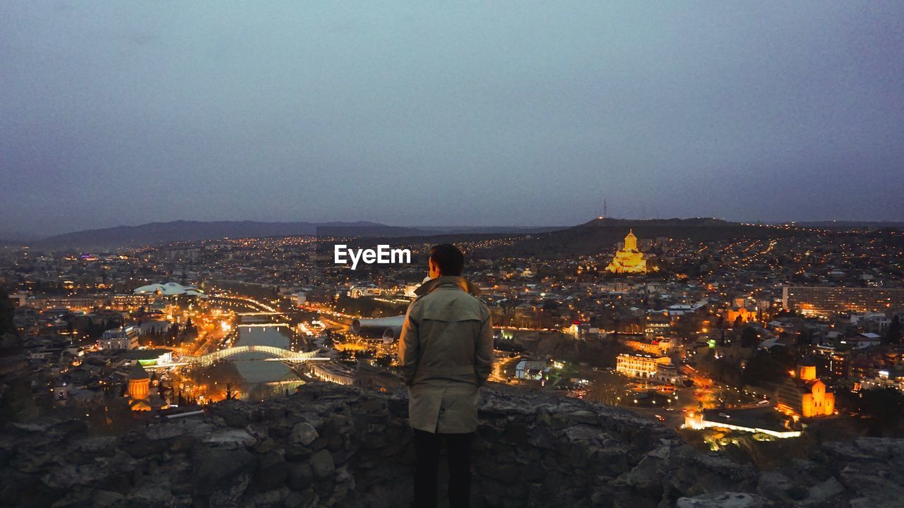 Rear view of man standing on mountain against sky at night