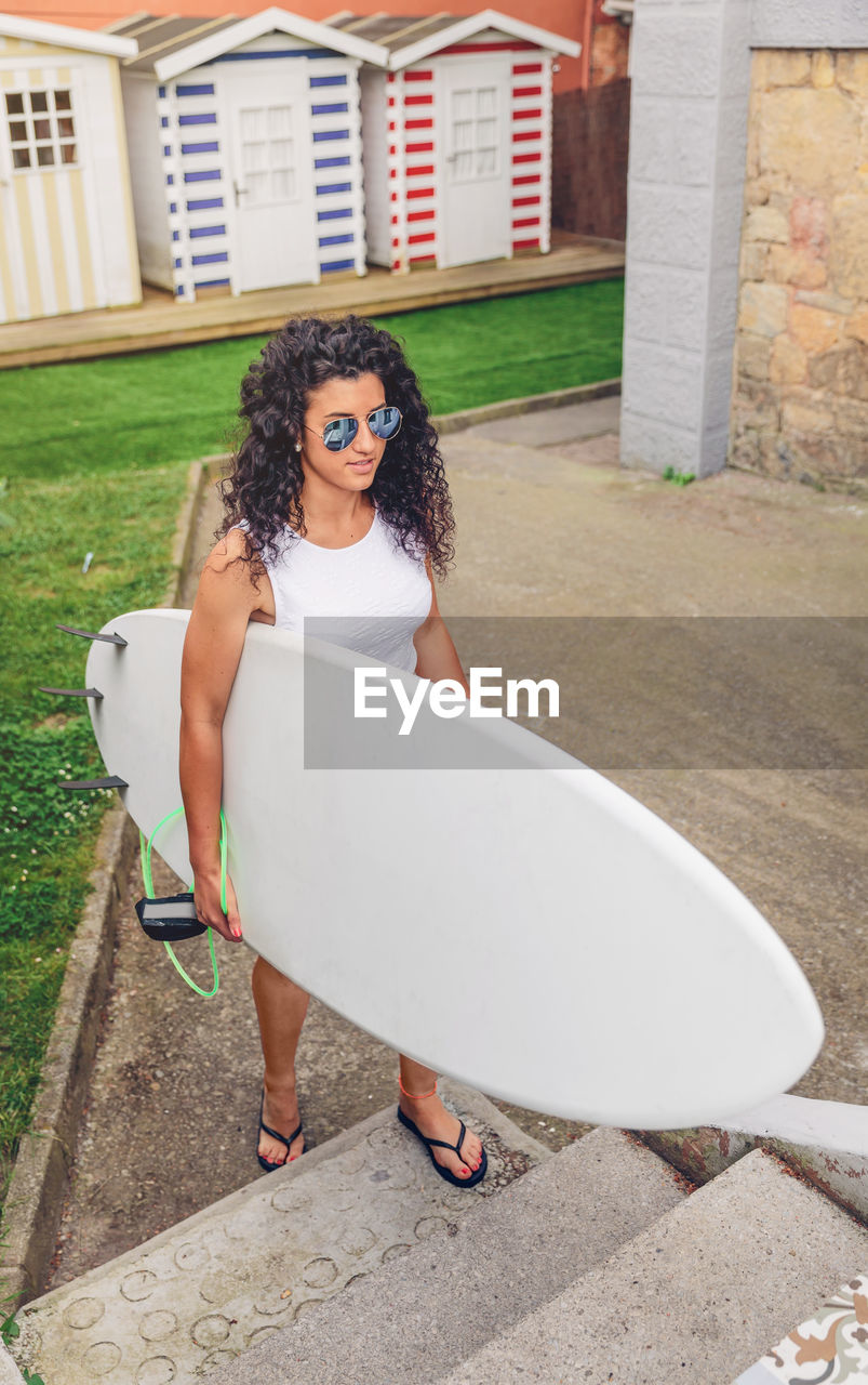 Young woman with surfboard standing against beach hut