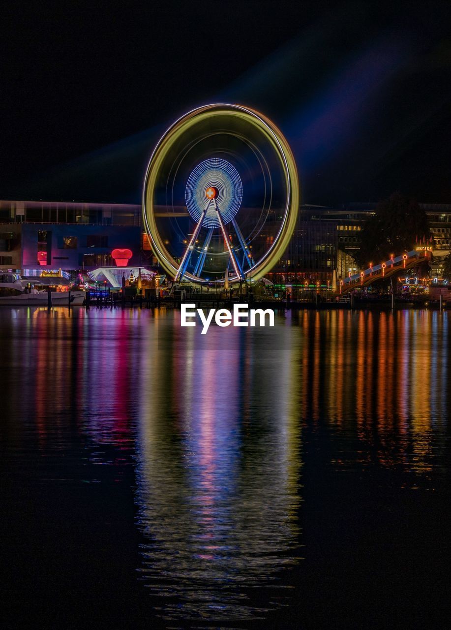 ILLUMINATED FERRIS WHEEL BY RIVER AT NIGHT