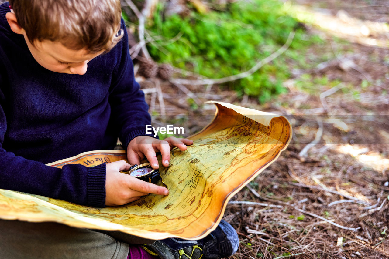 HIGH ANGLE VIEW OF BOY LOOKING AT WHILE SITTING ON LAND