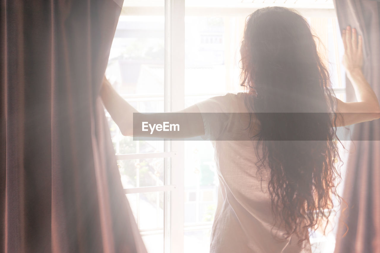 Rear view of woman standing by window at home