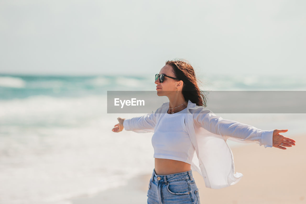 portrait of young woman wearing sunglasses while standing at beach