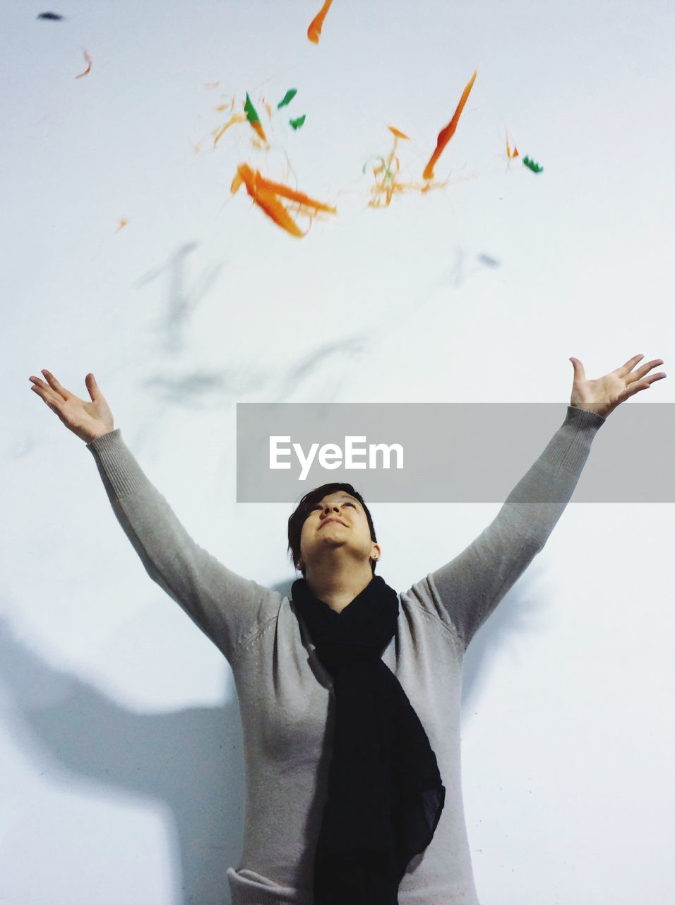 Young woman throwing colored particles against white background