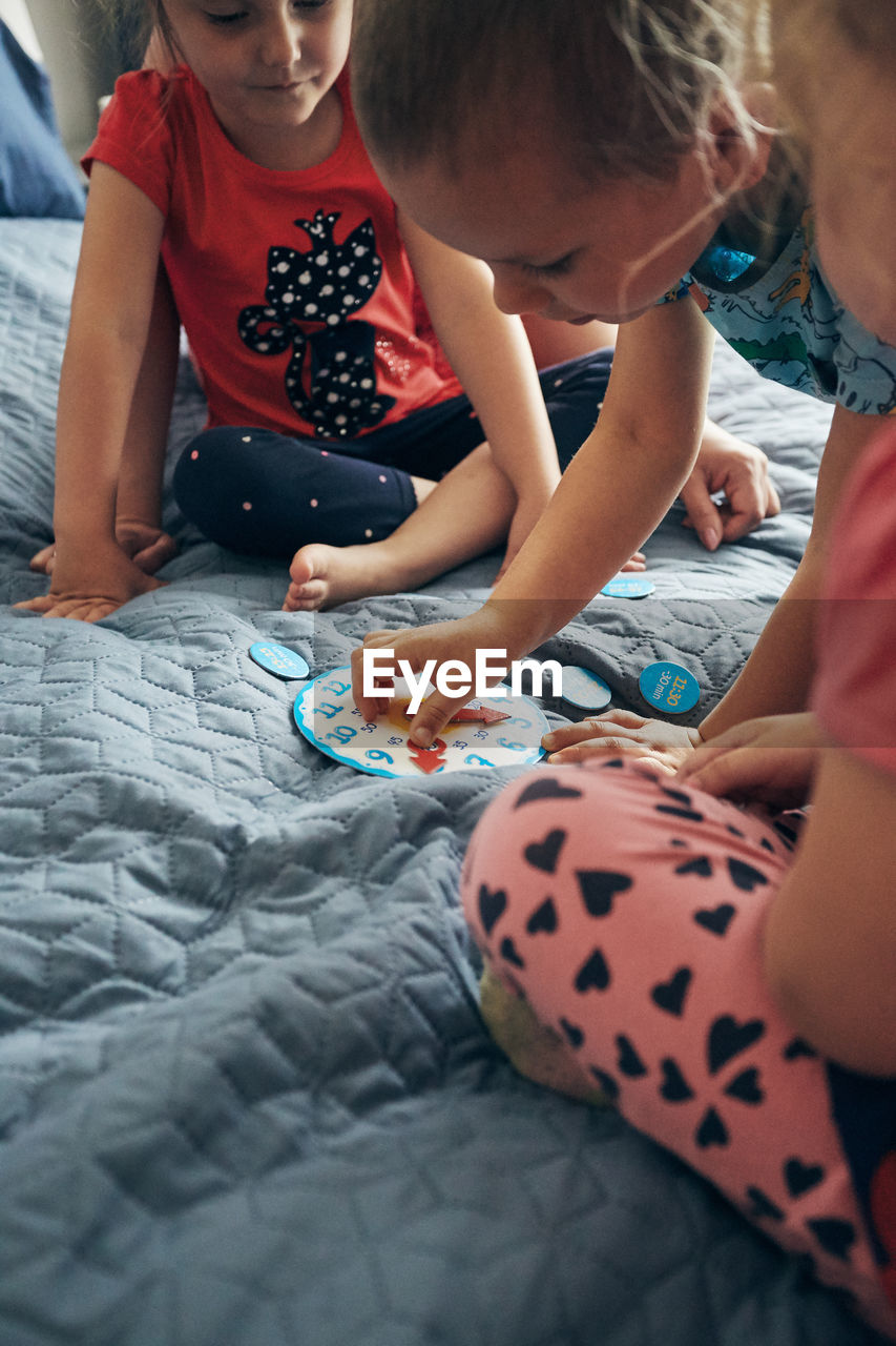 High angle view of people sitting by toy clock on bed