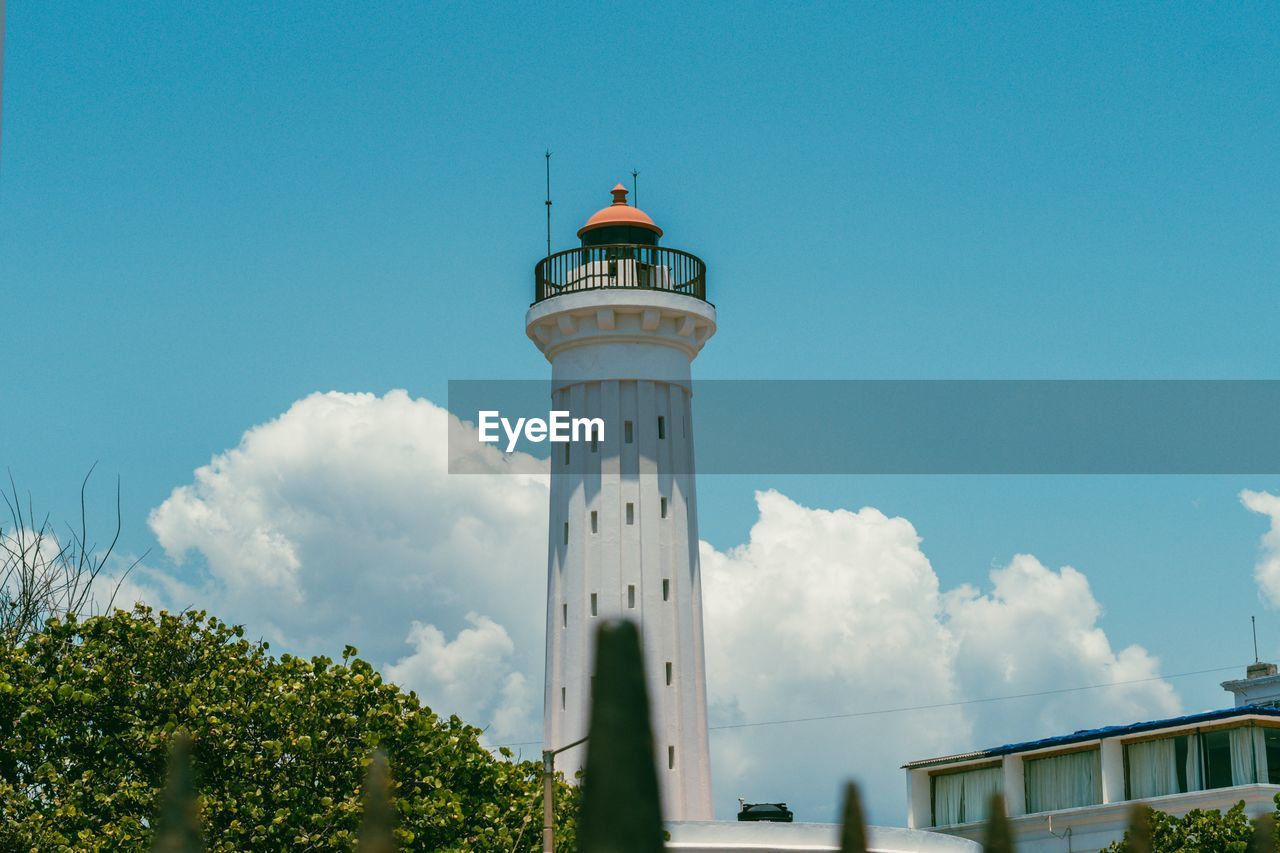 architecture, building exterior, built structure, lighthouse, tower, sky, building, guidance, nature, security, observation tower, protection, plant, day, travel destinations, blue, cloud, no people, travel, tree, outdoors, low angle view, house, tourism