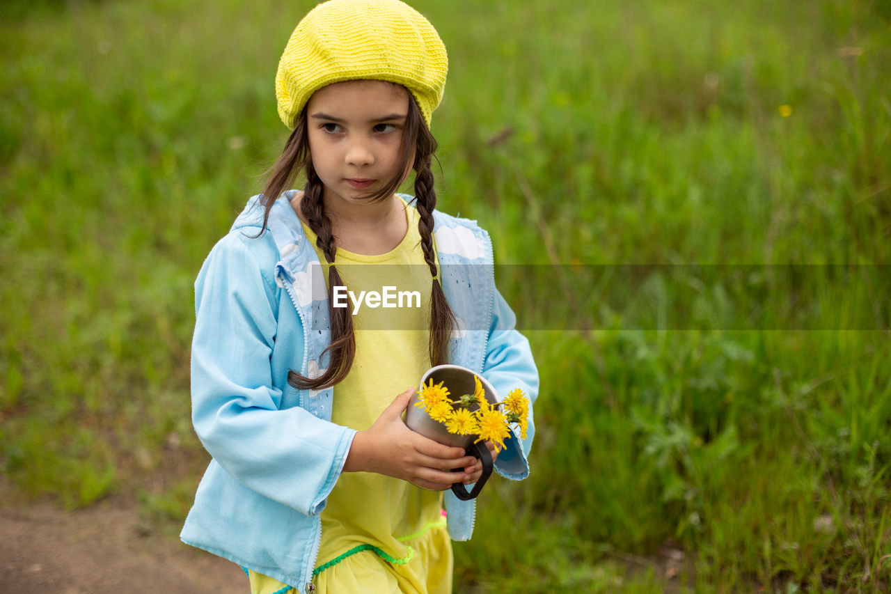 A little girl walks along a path near a green lawn with a bouquet of yellow dandelions