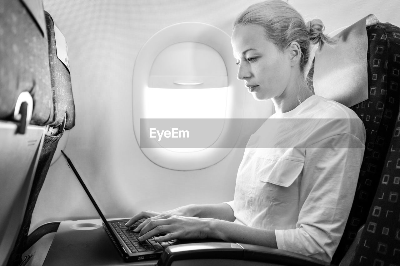 Side view of businesswoman working on laptop sitting at airplane