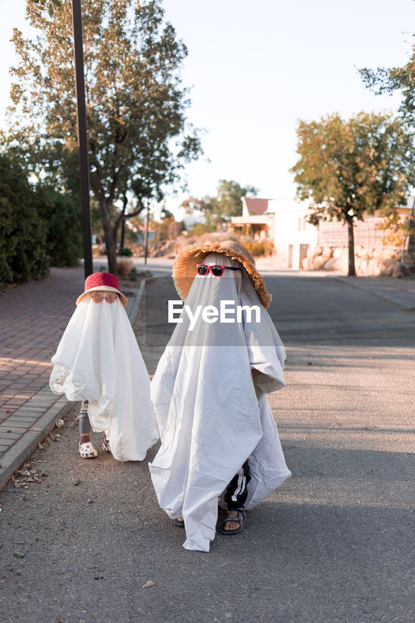 Trendy sheet ghosts costumes on little kids standing on a suburbs street. happy halloween holiday