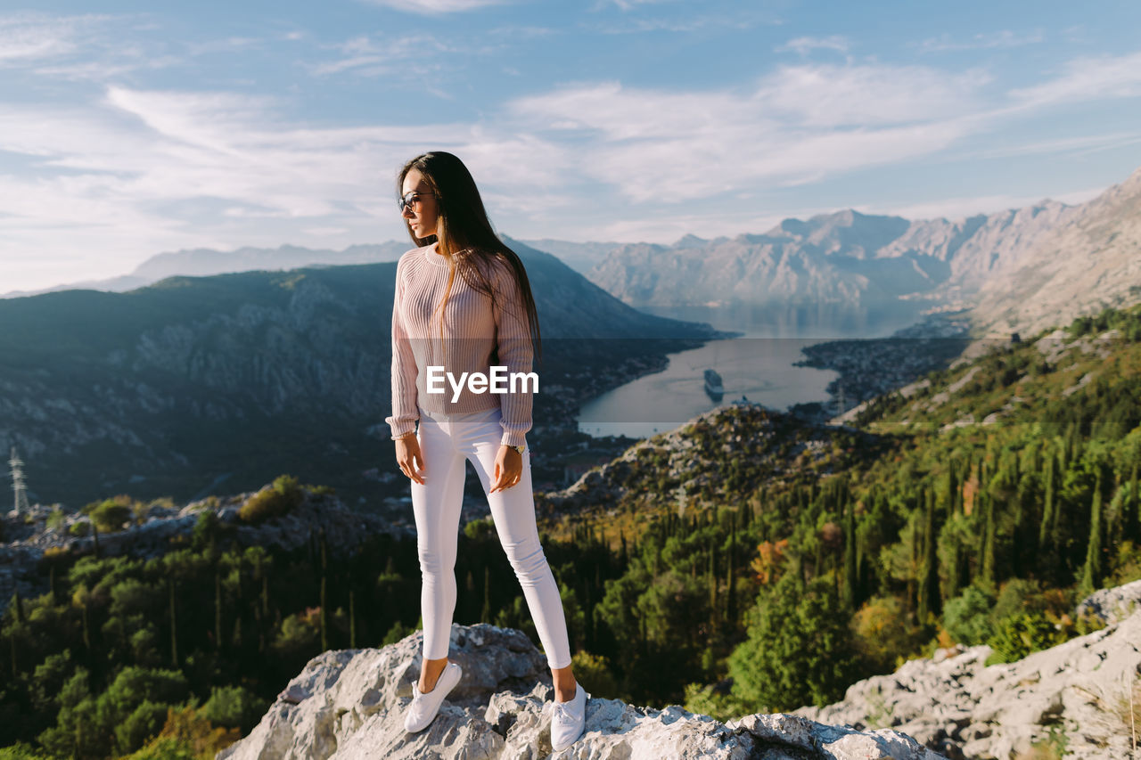 WOMAN STANDING ON ROCK AGAINST MOUNTAINS