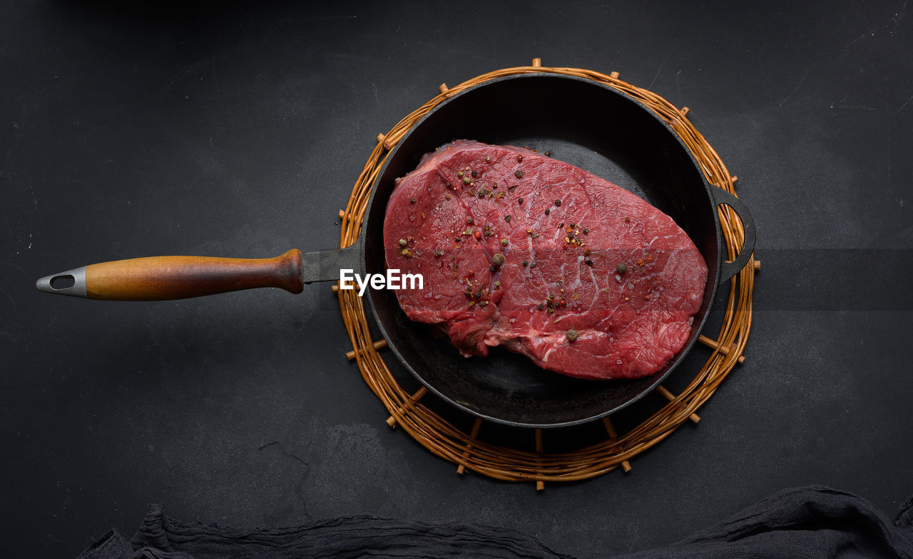 Raw beef tenderloin lies in a metal round frying pan on a black table, top view