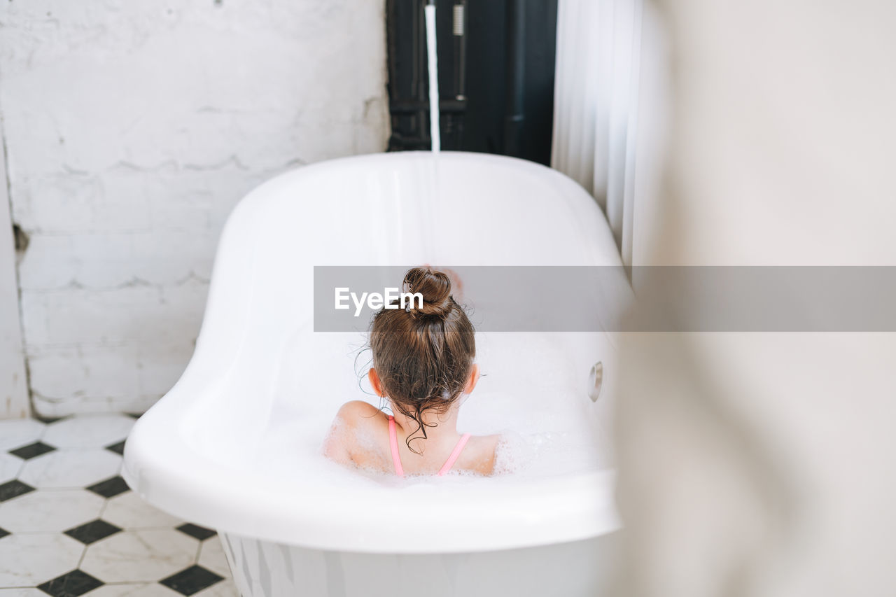 Happy little girl having fun in bath with foam at home