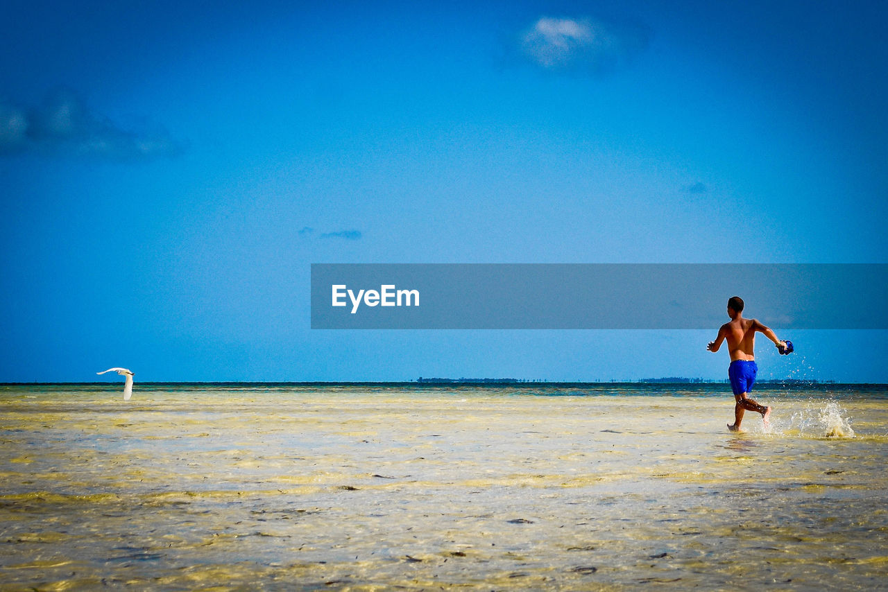 FULL LENGTH OF SHIRTLESS MAN ON BEACH