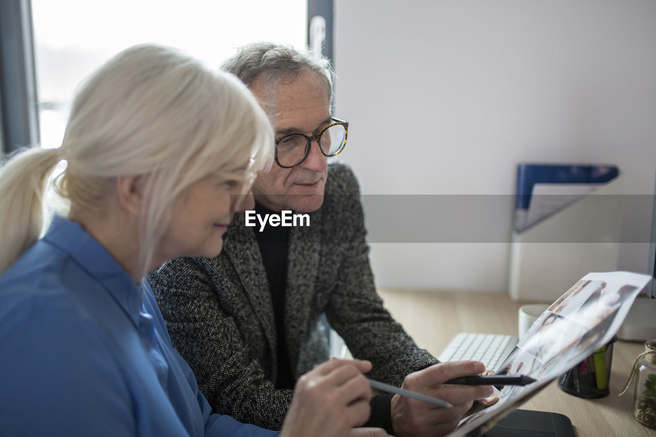 Two senior colleagues working together at desk in office examining photos