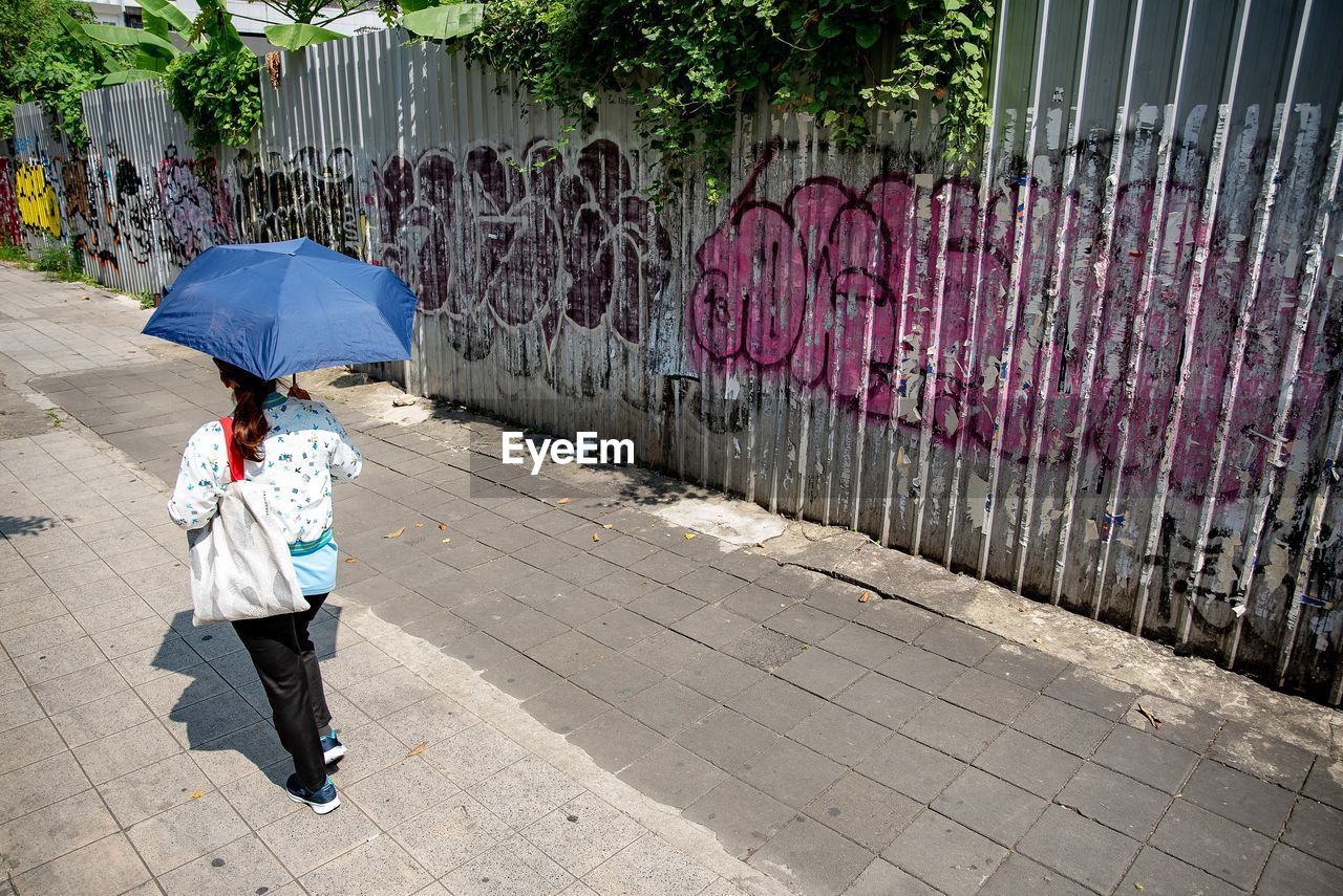 FULL LENGTH REAR VIEW OF WOMAN WALKING ON FOOTPATH