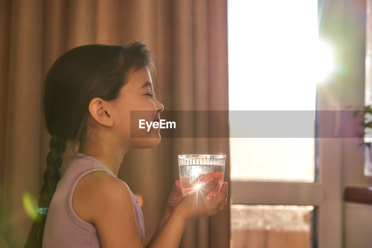 Girl drinks water from a glass in the sun. back light.