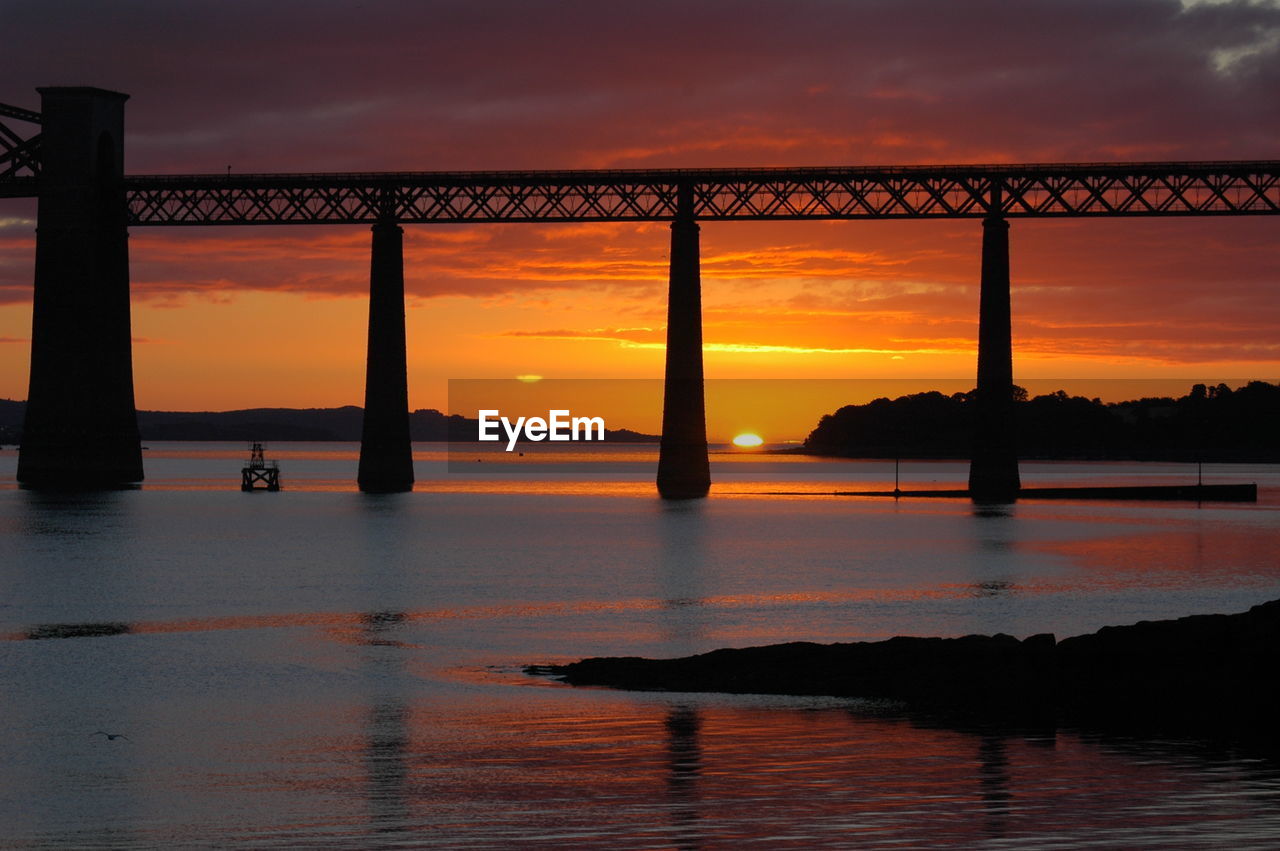 Silhouette bridge over river against sky during sunset