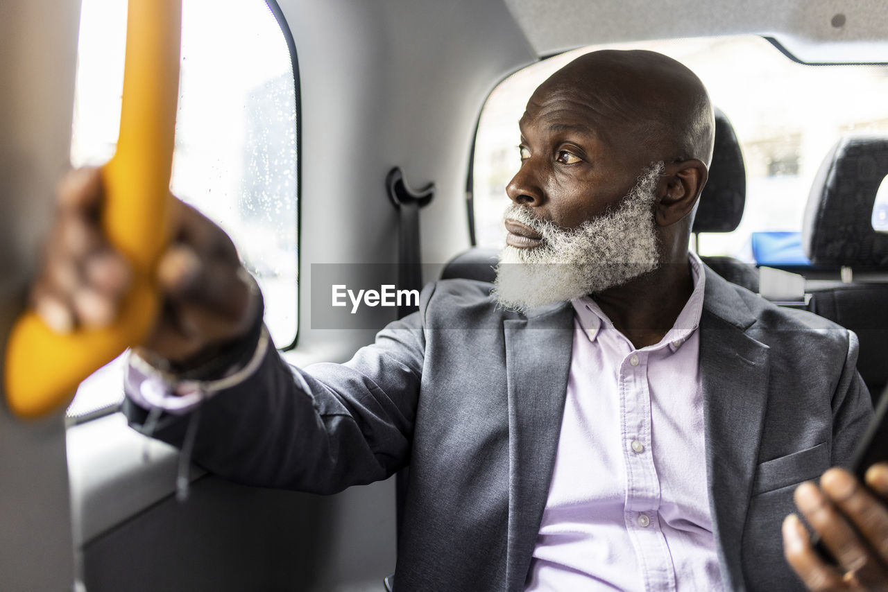 Senior businessman holding handle and looking through taxi window